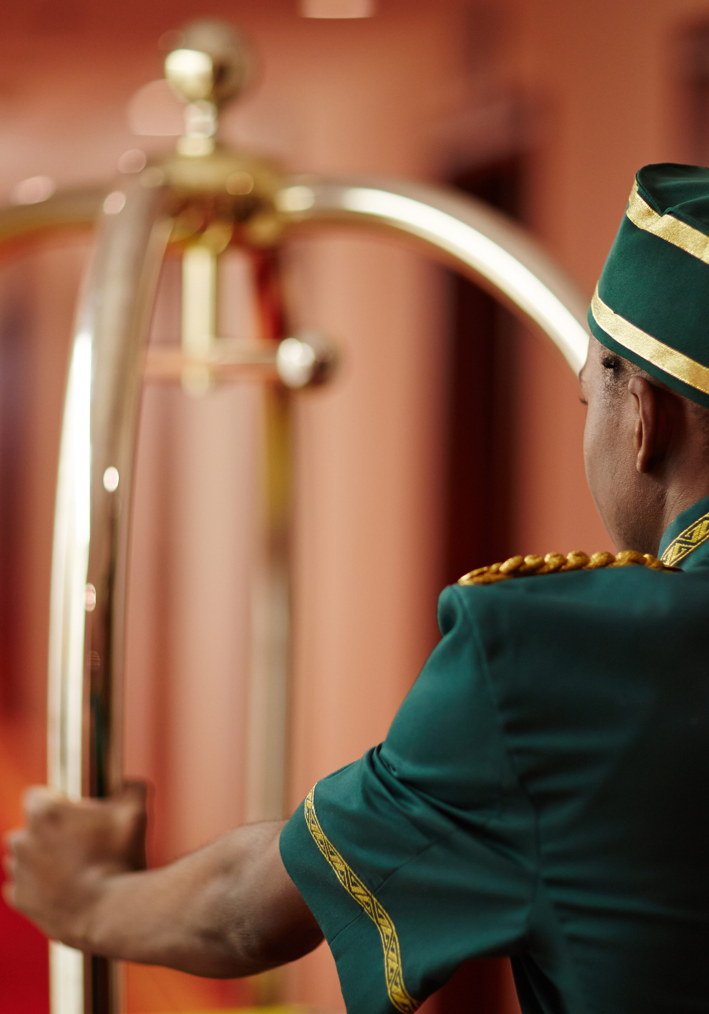 A hotel bellhop in uniform holding a luggage cart.